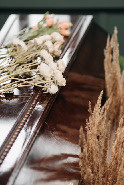 A delicate bouquet of white dried flowers with small, round blossoms and slender stems is laid across the polished surface of a dark wooden piano. The flowers are wrapped in soft paper, tied with a su